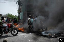 Yon taksi-moto pase bo kote yon barikad kawotchou kap boule pandan yon manifestasyon chofe taksi yo nan Potoprens, pou pwoteste kont rate gaz la, Mekredi 13 Jiye, 2022.