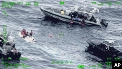 This photo released by the Seventh U.S. Coast Guard District shows people standing on a capsized boat, left, as some of its passengers are pulled up on to a rescue boat, top, in the open waters northwest of Puerto Rico, May 12, 2022. 