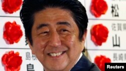 Thủ tướng Nhật Bản Shinzo Abe mĩm cười khi ông cài bông hồng nhỏ bằng ruy băng lên bảng tên của một ứng cử viên được dự kiến đắc cử, 21/7/13