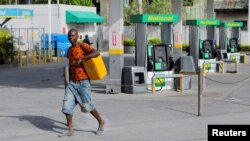 Yon mesye pote yon galon gazolin ki vid pandan lap pase bo kote yon stasyon gaz ki femen nan Potoprens, Ayiti, 13 Jiye, 2022. 