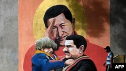 Một người đi ngang qua tranh tường vẽ cố TT Hugo Chavez, giữa, giơ tay chào TT Nicolas Maduro, phải, đang bồng một đừa trẻ ở Caracas. (Photo by Federico PARRA / AFP)