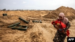 A Palestinian holding a baby walks past ammunition containers left behind by Israeli troops as she flees Khan Yunis in the southern Gaza Strip further south on February 2, 2024, amid ongoing battles between Israel and the militant group Hamas.