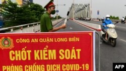 Một công an đứng canh tại một chốt kiểm soát ở Hà Nội ngày 29/7/2021. Bộ Y tế Việt Nam vừa quyết định giảm thời gian cách ly tập trung cho người nhập cảnh đã tiêm vaccine đầy đủ xuống còn 7 ngày.