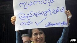 Bà Suu Kyi giơ cao tấm bảng "Tôi cũng yêu mọi người" cho những người ủng hộ bà tại trụ sở của NLD ở Yangon, Miến Điện, 14/11/2010