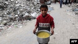 Gazzeli bir çocuk yardım kuruluşunun sağladığı bir tencere iftar yemeğiyle enkaz yığınları arasında yürürken