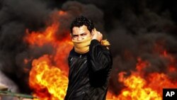 A protester stands in front of a burning barricade during a demonstration in Cairo, Jan 28, 2011