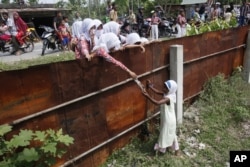 Học sinh Aceh đưa thực phẩm cho một bé gái Rohingya từ bên ngoài hàng rào của trại tị nạn tạm thời ở Bayeun, tỉnh Aceh.