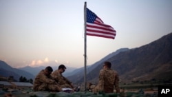 FILE - In this Sept. 11, 2011 photo, US soldiers sit beneath an American flag just raised to commemorate the tenth anniversary of the 9/11 attacks at Forward Operating Base Bostick in Kunar province, Afghanistan. 