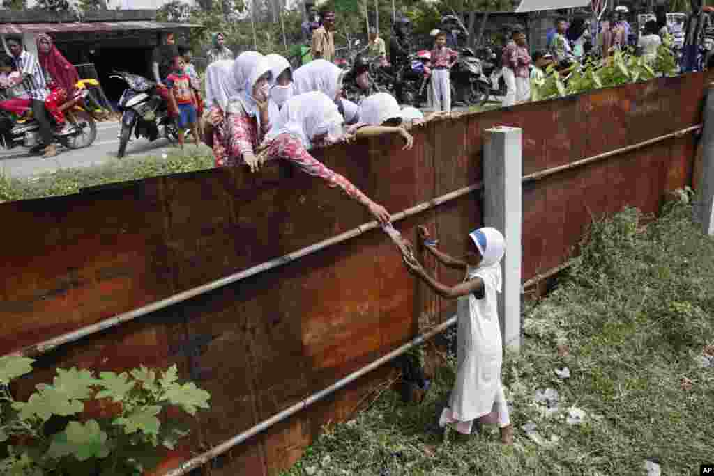 Các học sinh Indonesia đưa thực phẩm cho một bé gái Rohingya từ bên ngoài hàng rào của&nbsp;nơi trú ẩn tạm thời cho di dân ở Bayeun, tỉnh Aceh, Indonesia, ngày 21/5/2015.