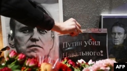 A person places a placard reading 'Putin killed Navalny!' as people pay tribute to late Russian opposition leader Alexei Navalny at a makeshift memorial in front of the Russian Embassy in Warsaw on March 1, 2024, following his funeral ceremony at the Bori