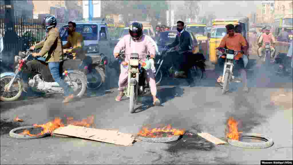 مظاہرین کی جانب سے جلائے گئے ٹائرز کے قریب سے گزرتے موٹر سائیکل سوار